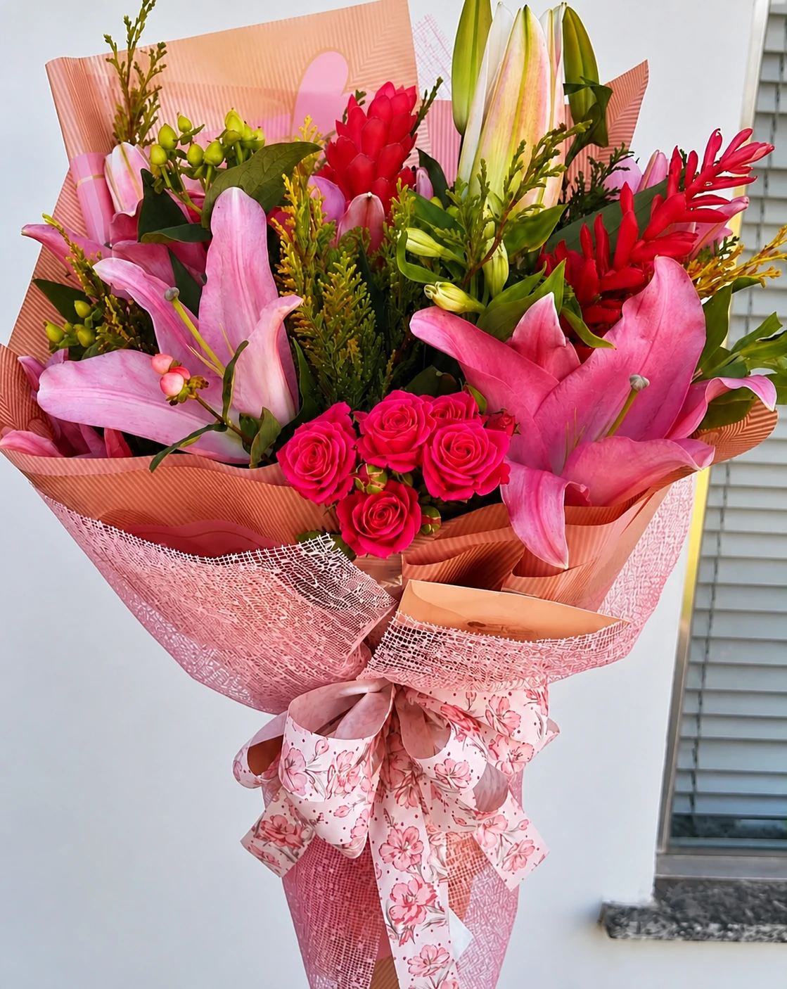Buquê real em tons de rosa com lírios, rosas e folhagens, preparado pela Flores do Campo